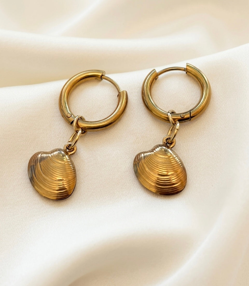 Dainty gold hoop earrings with mini sea shell charms hanging from hoops for a beachy look.